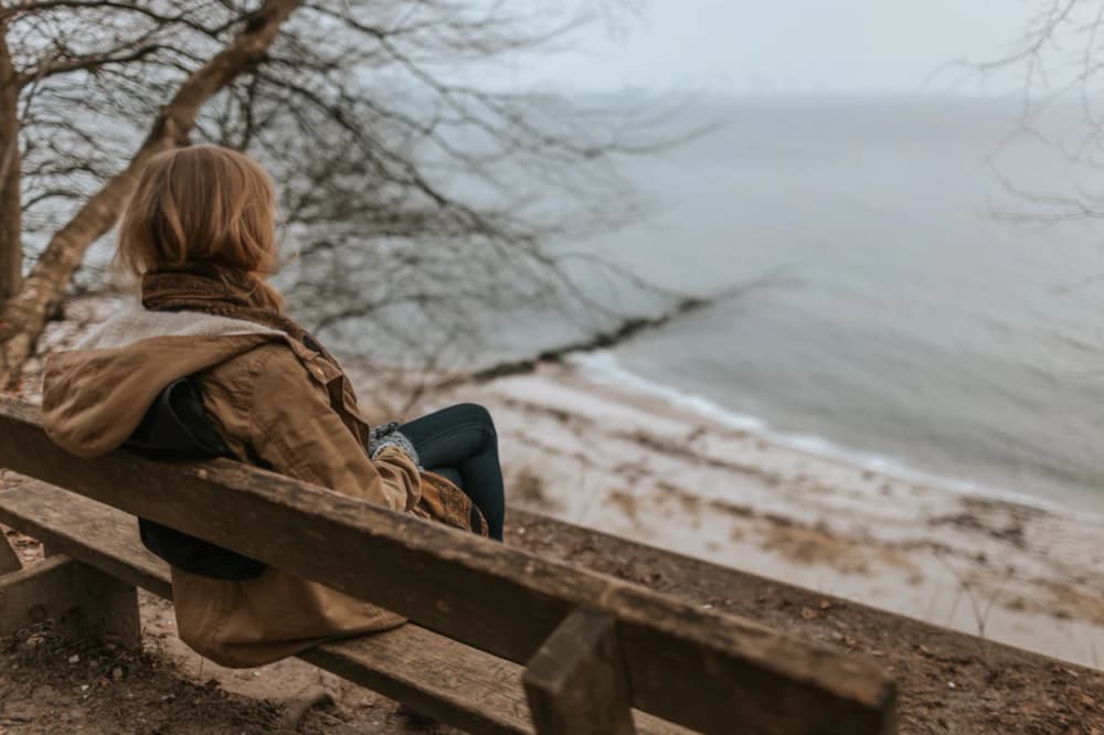 A woman sitting on bench looking at a lake